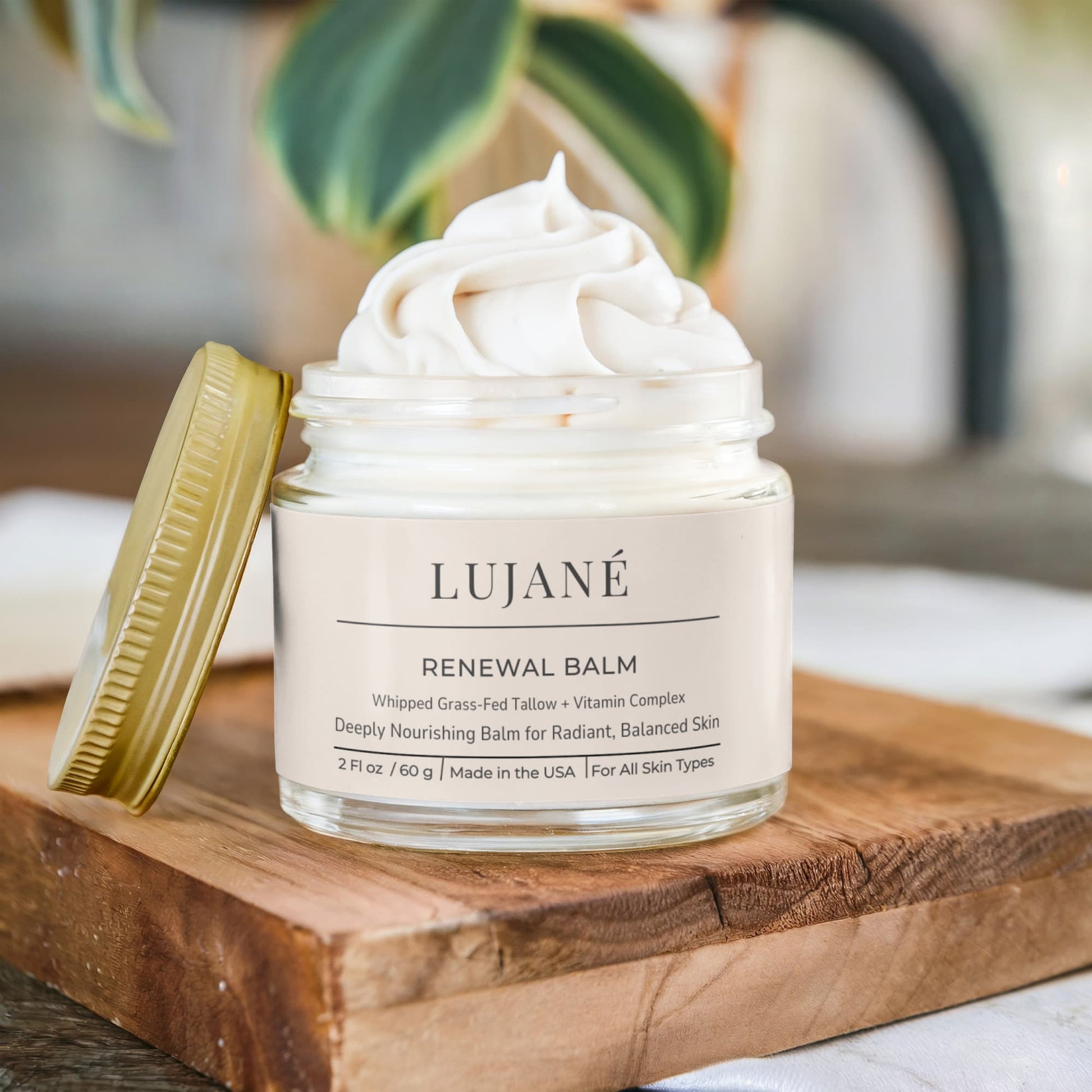 An open jar of LUJANÉ Renewal Balm showing a luminous, whipped tallow texture on a rustic wooden surface, highlighting the radiant glow and deep hydration benefits of this luxury natural moisturizer.